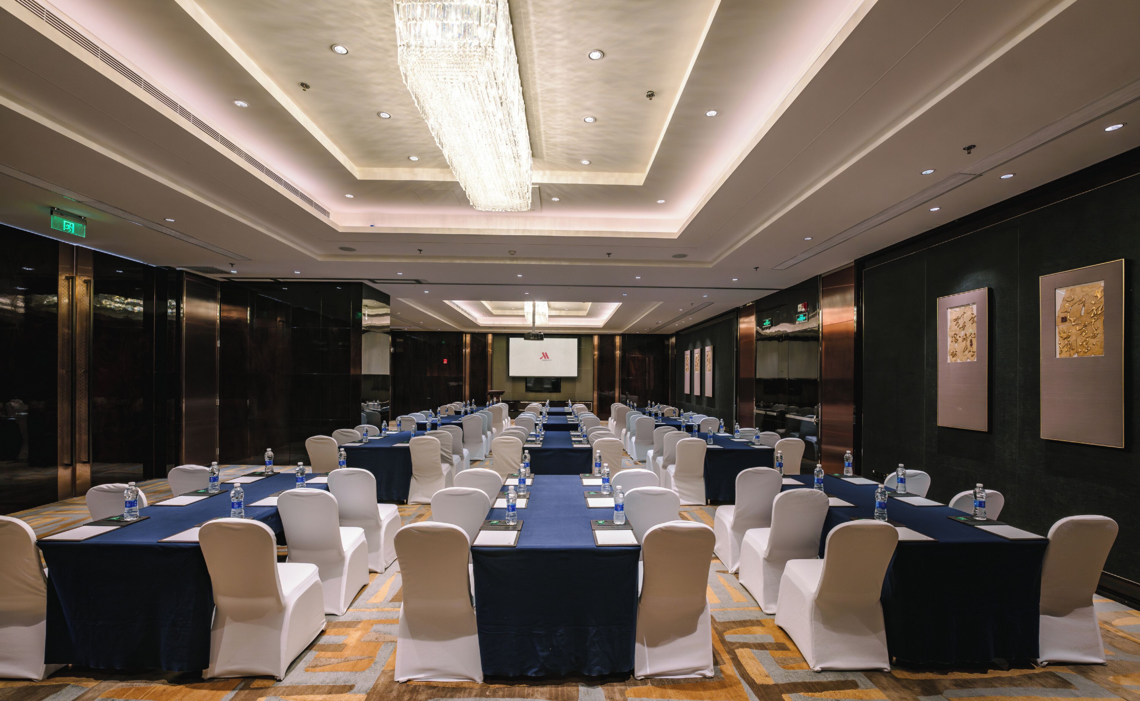 Un salón de conferencias con varias mesas, sillas y una pantalla grande al frente.