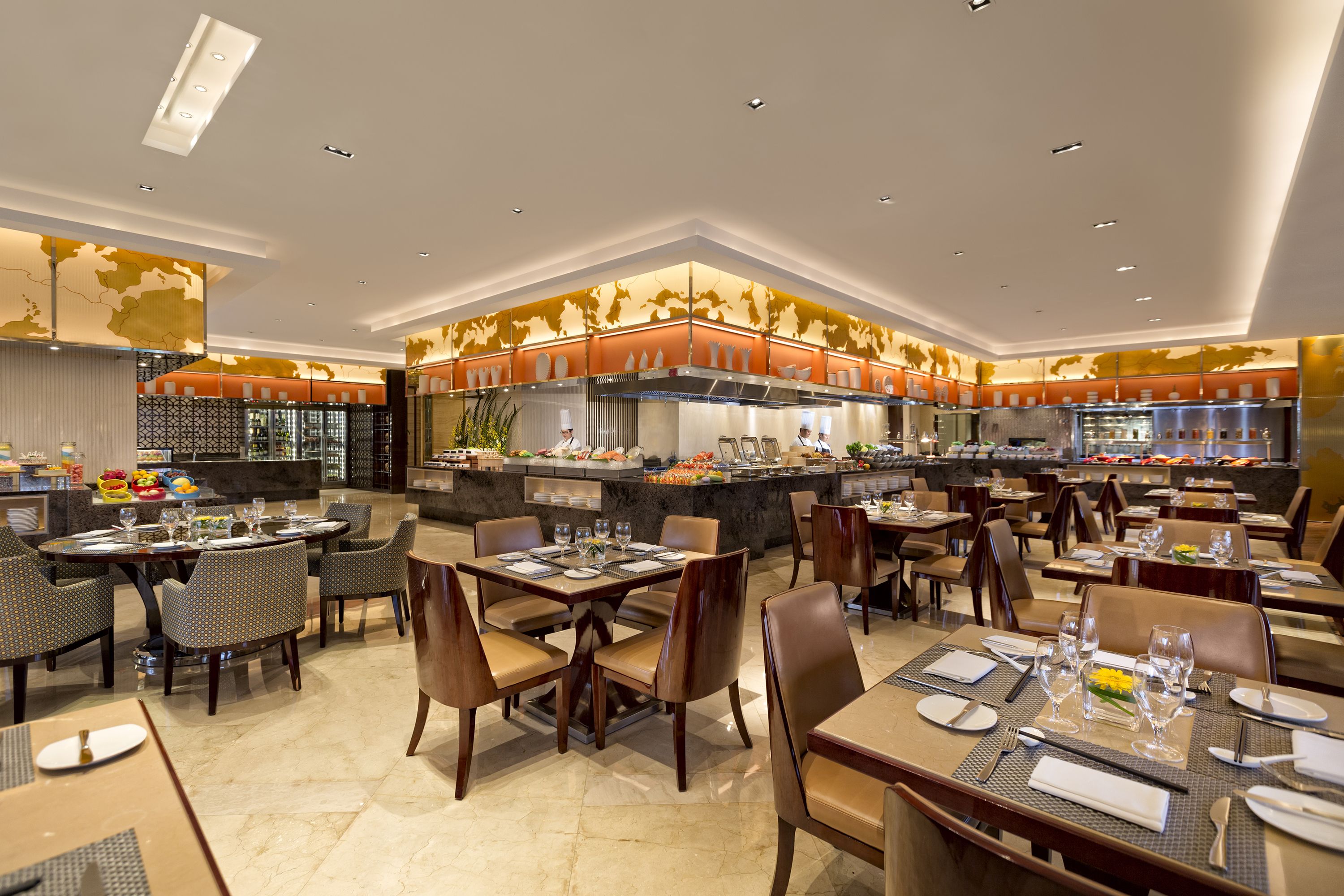 A spacious restaurant with multiple dining tables and chairs, a central bar area, and a modern kitchen in the background.