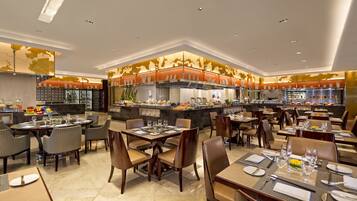 A spacious restaurant with multiple dining tables and chairs, a central bar area, and a modern kitchen in the background.
