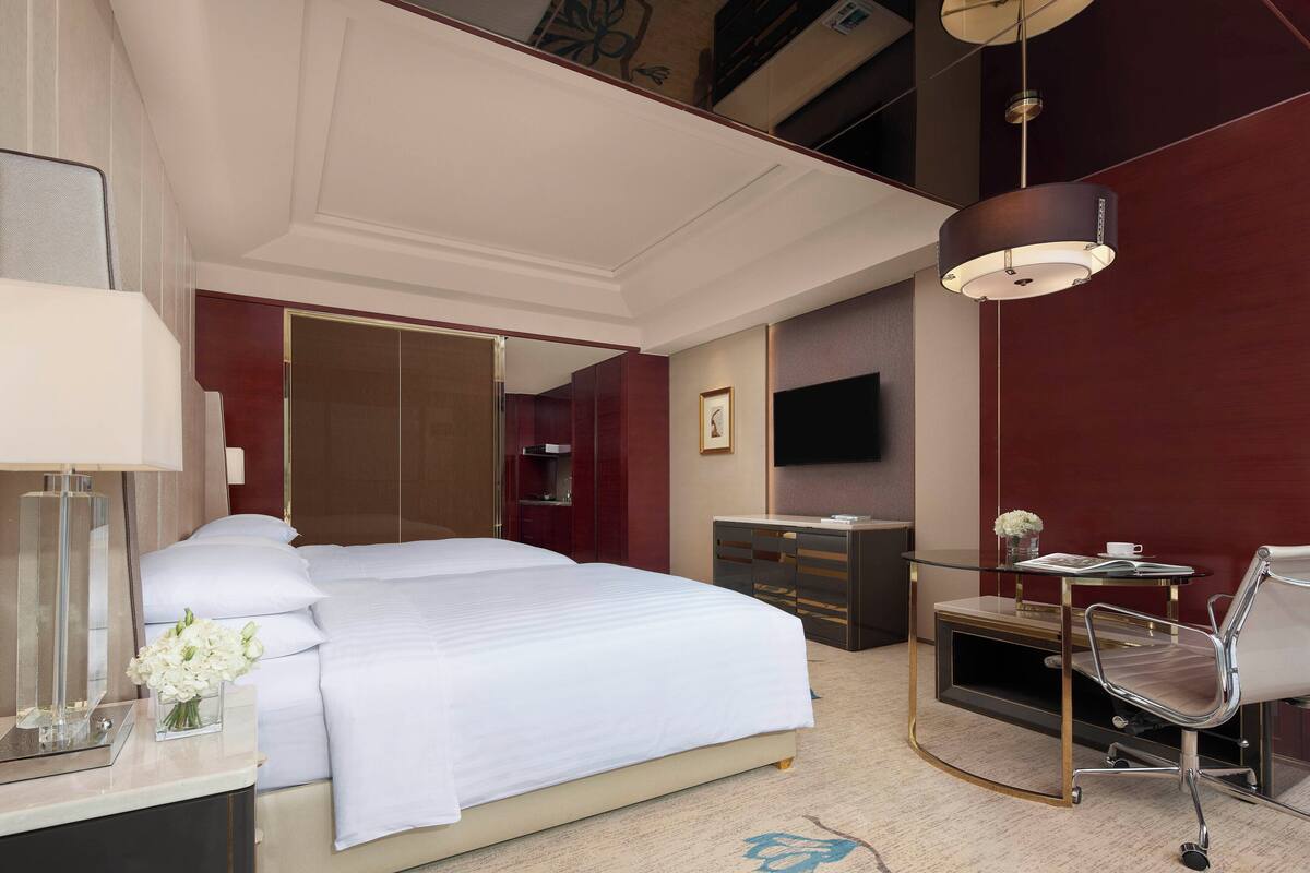 A hotel room with a large bed, a desk with a chair, a television, and a wardrobe.