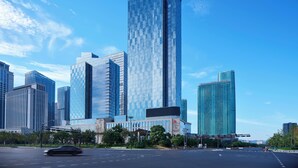 Paisagem urbana moderna com arranha-céus imponentes, céu azul límpido e rua arborizada bem cuidada.