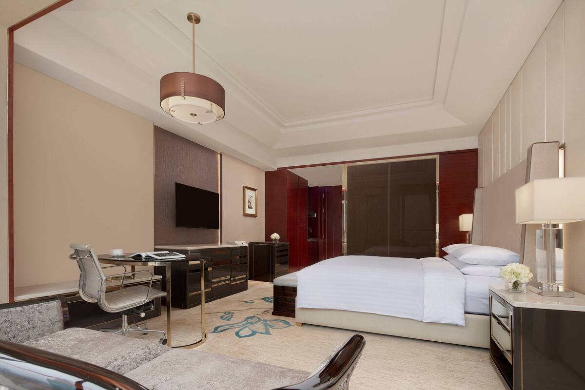 A hotel room with a bed, desk, chair, and a television.
