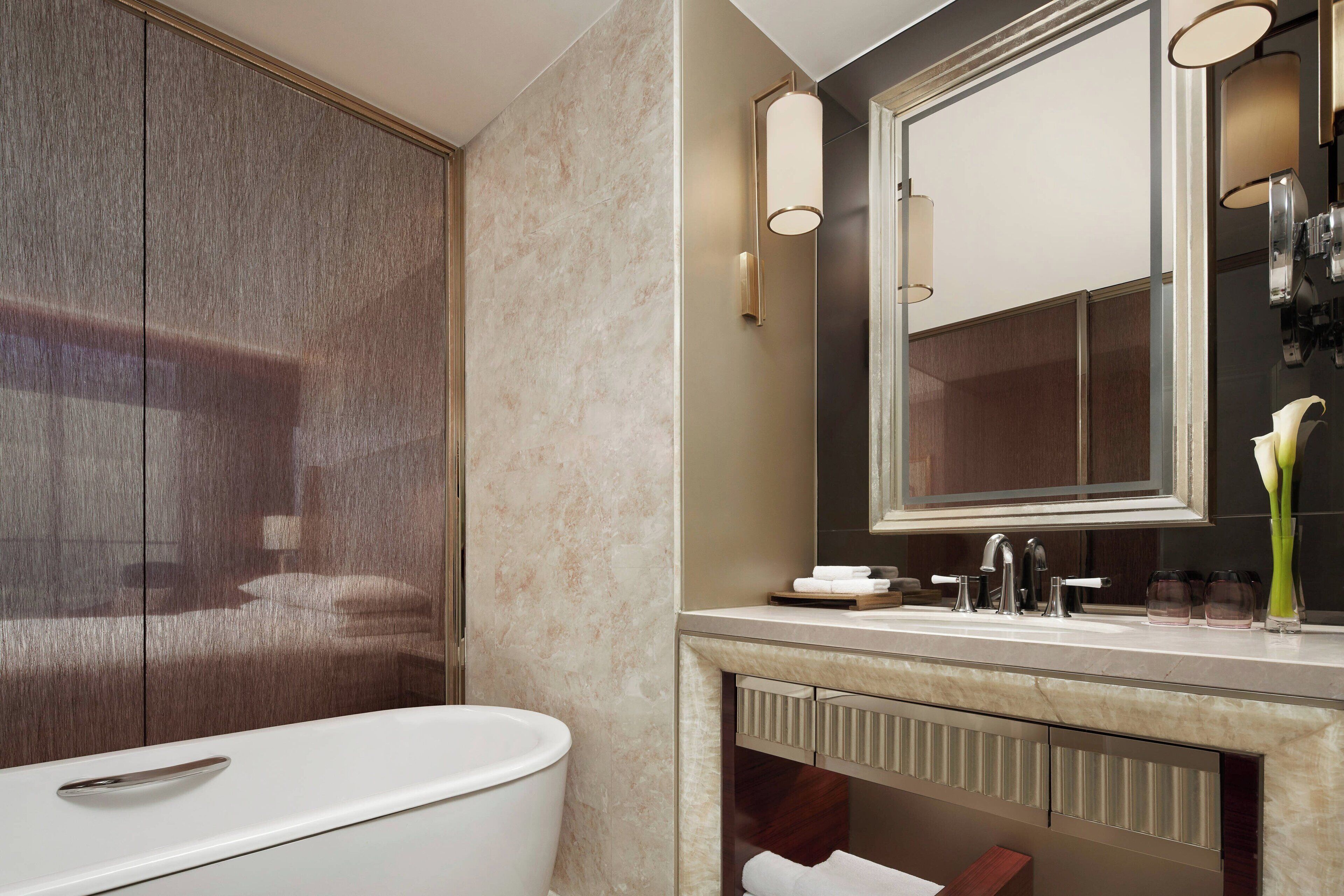 Un baño moderno con un espejo grande, una bañera y un mueble de tocador con lavabo y toallero.
