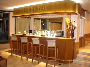 A lobby bar with a wooden counter, bar stools, and a variety of bottles.