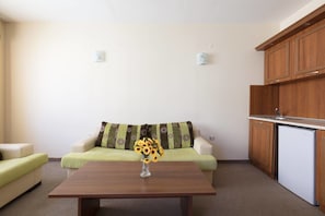 A living room with a sofa, a coffee table, and a small kitchen area with wooden cabinets and a refrigerator.