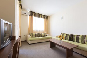 A living room with a flat-screen TV, two sofas, a coffee table, and a window with curtains.