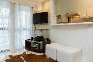 A modern living room with a flat-screen TV mounted on the wall, a white sofa, a small entertainment unit, and a cowhide rug.