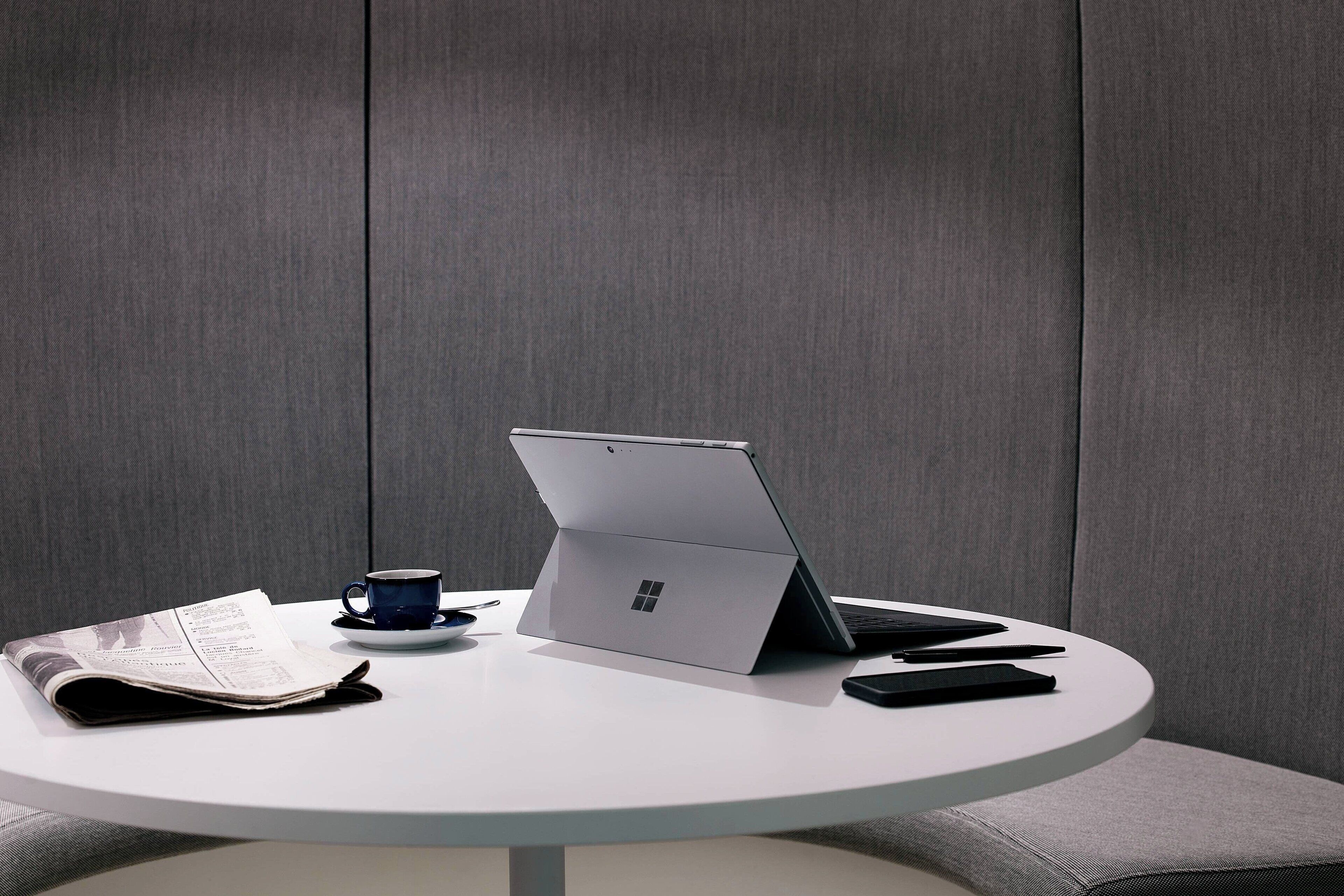 A laptop on a white table with a cup and a newspaper.