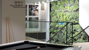A pool table with a cue stick and billiard balls, a staircase with a metal railing, and a green wall with plants. - Courtyard by  Marriott Paris Gare de Lyon (Paris)