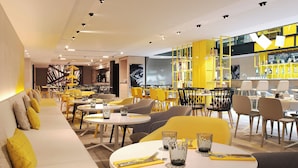 A modern restaurant interior with yellow and grey seating, white tables, and a bar area with yellow shelving. - Courtyard by  Marriott Paris Gare de Lyon (Paris)