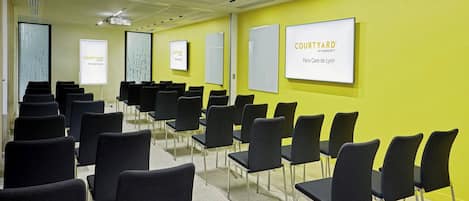 A conference room with rows of black chairs, a projector screen, and a sign reading "COURTYARD Paris Gare de Lyon".