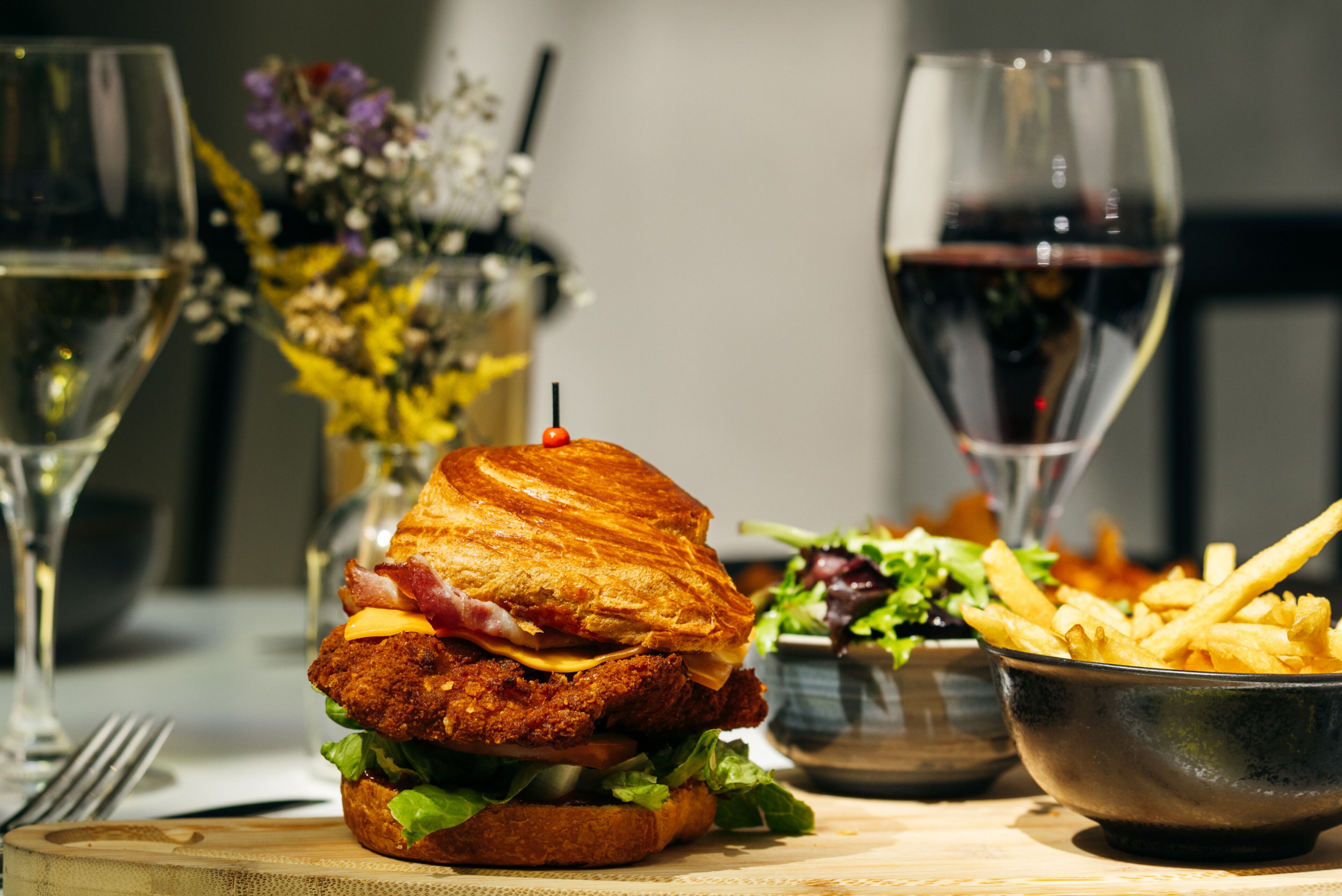 Una comida con un sándwich, papas fritas y una copa de vino tinto sobre una mesa.