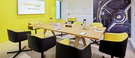 A conference room with a large table, yellow and black chairs, a sign reading "COURTYARD Paris Gare de Lyon", and a large abstract painting on the wall.