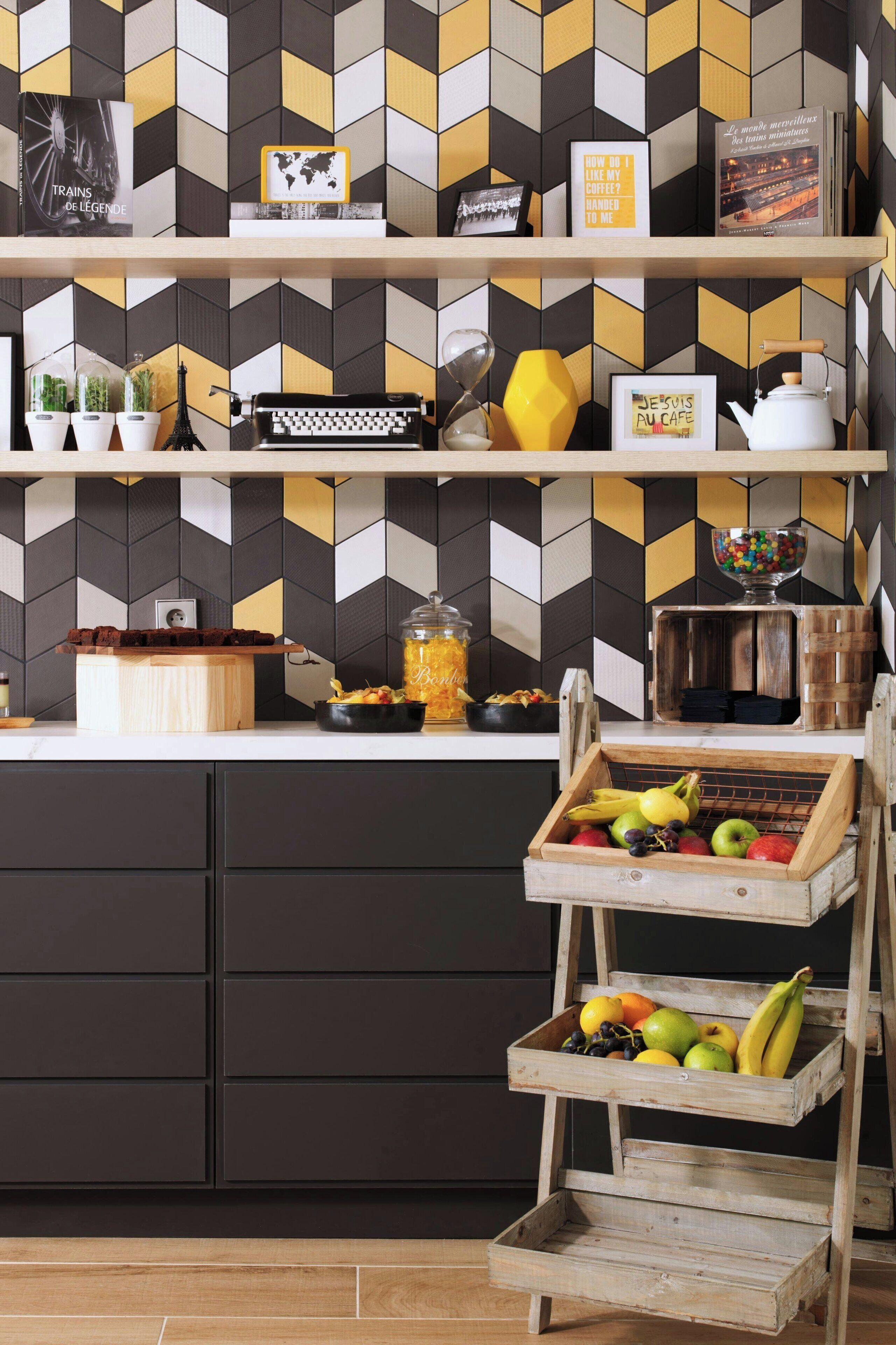 A kitchen with a geometric patterned backsplash, wooden shelves with various items, and a fruit basket on a wooden stand.