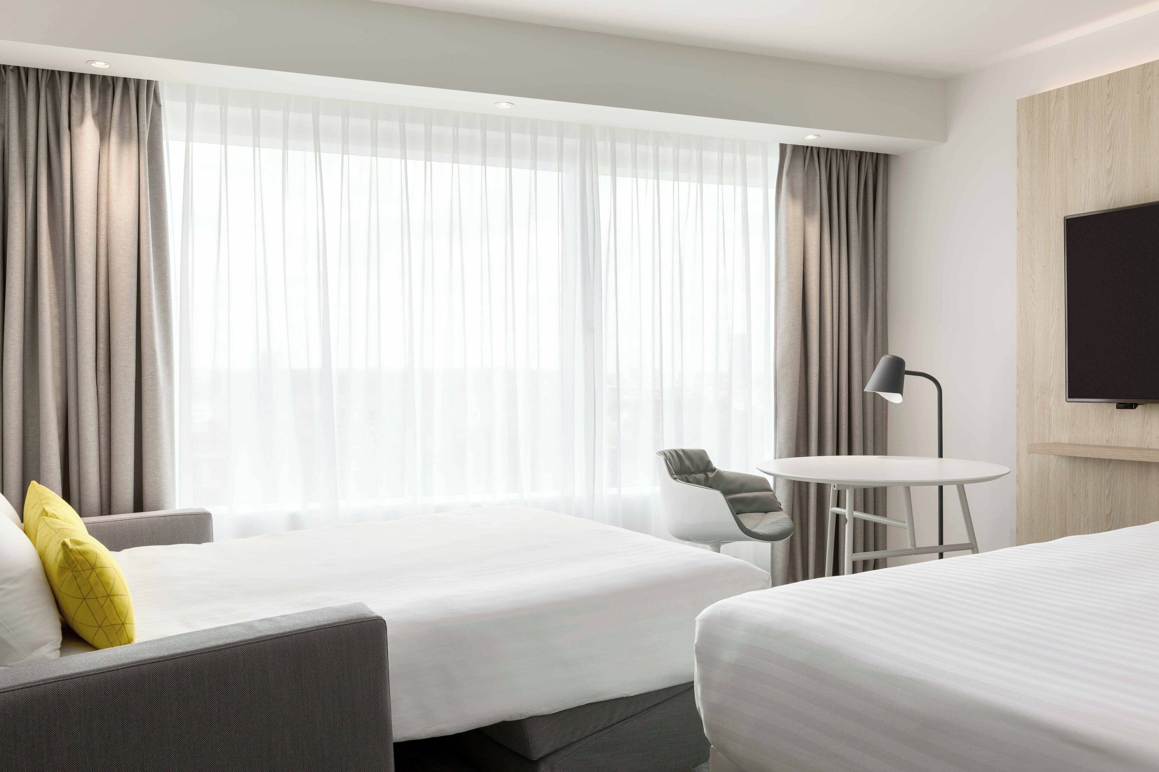 Ein Hotelzimmer mit zwei Betten, einem Schreibtisch, einem Stuhl und einem Fernseher.