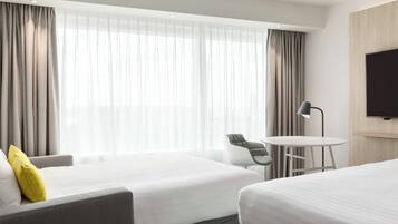 Ein Hotelzimmer mit zwei Betten, einem Schreibtisch, einem Stuhl und einem Fernseher.