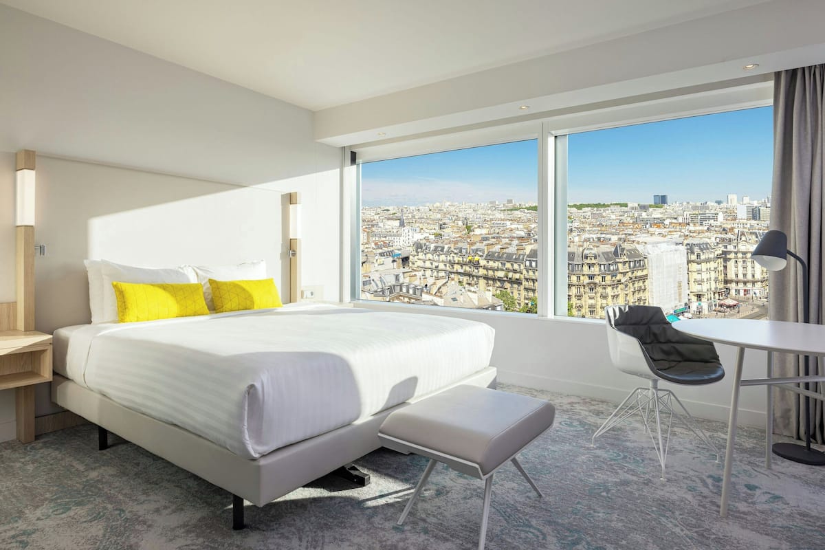 Une chambre d’hôtel moderne avec un grand lit, un bureau et une vue sur le paysage urbain.