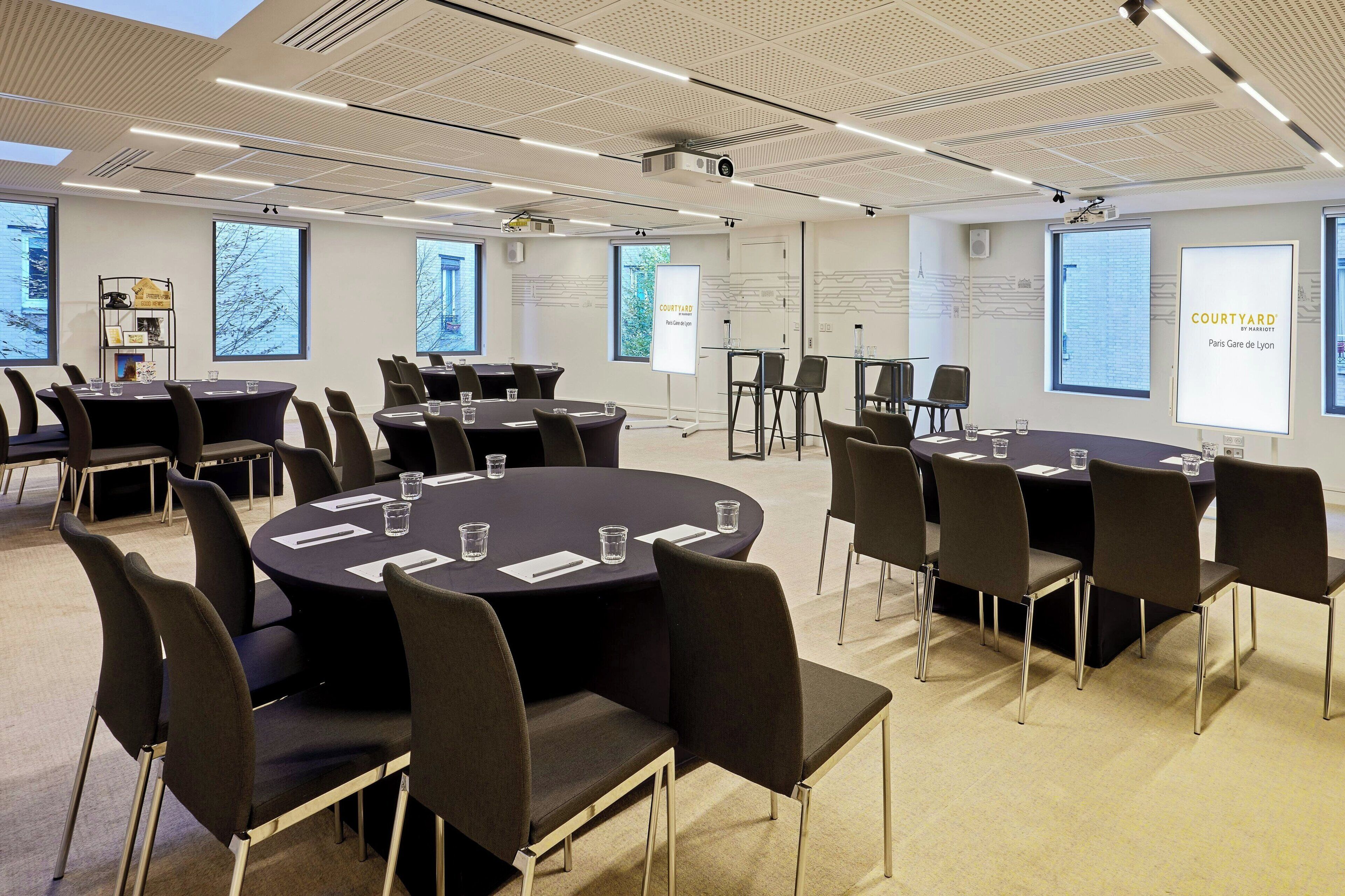 A conference room with multiple tables and chairs, large windows, and presentation screens.