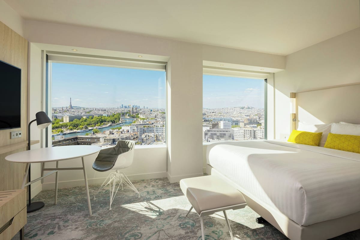 Une chambre d’hôtel dotée d’une grande fenêtre donnant sur la ville, d’un lit, d’un bureau et d’une chaise.