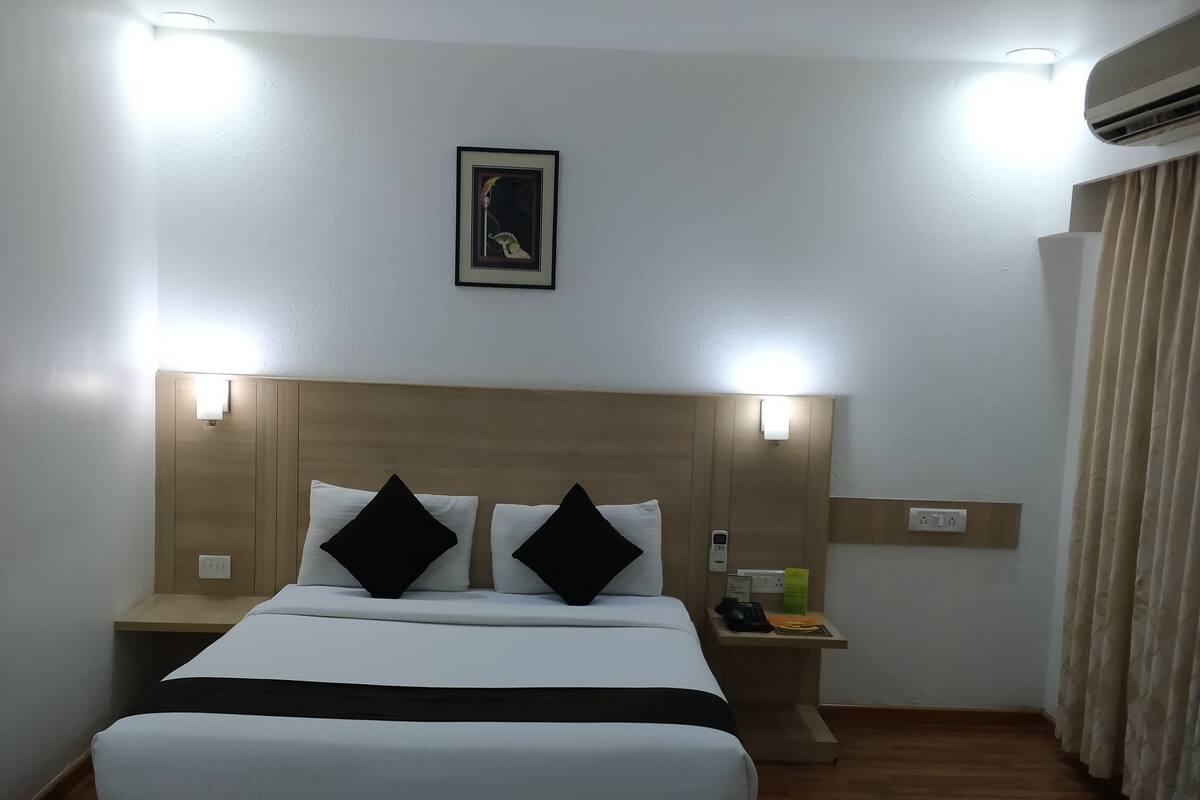 Una habitación de hotel con cama, mesitas de noche, aire acondicionado de pared y un cuadro en la pared.