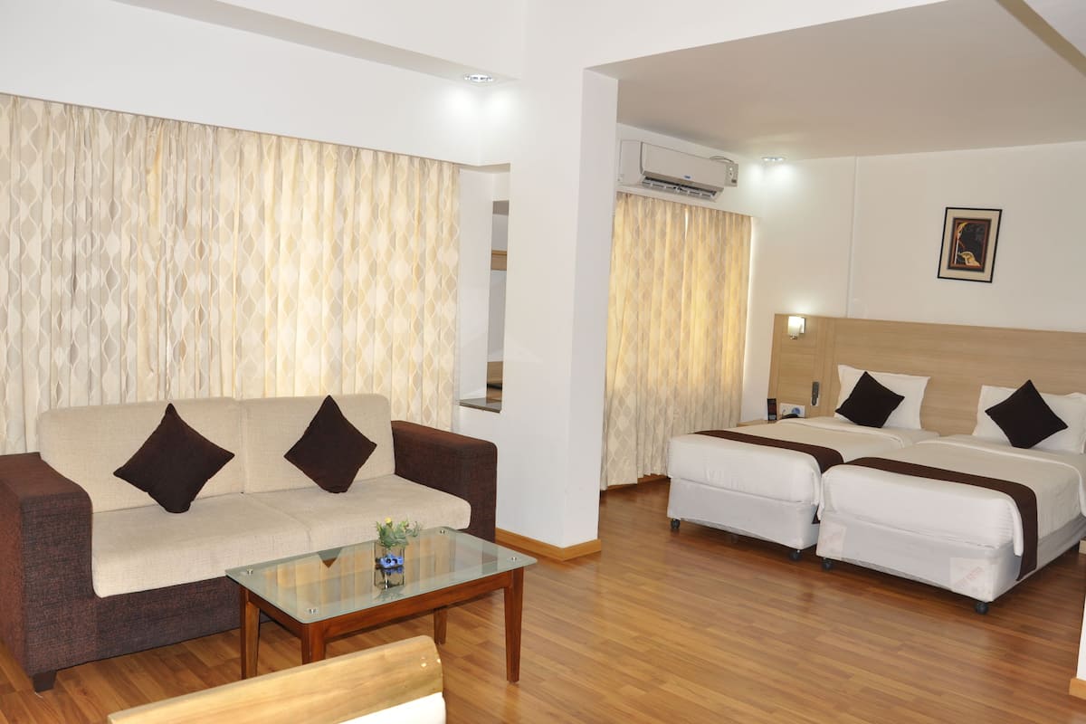 Habitación de hotel con sofá, dos camas, una mesa de centro de vidrio y un equipo de aire acondicionado.