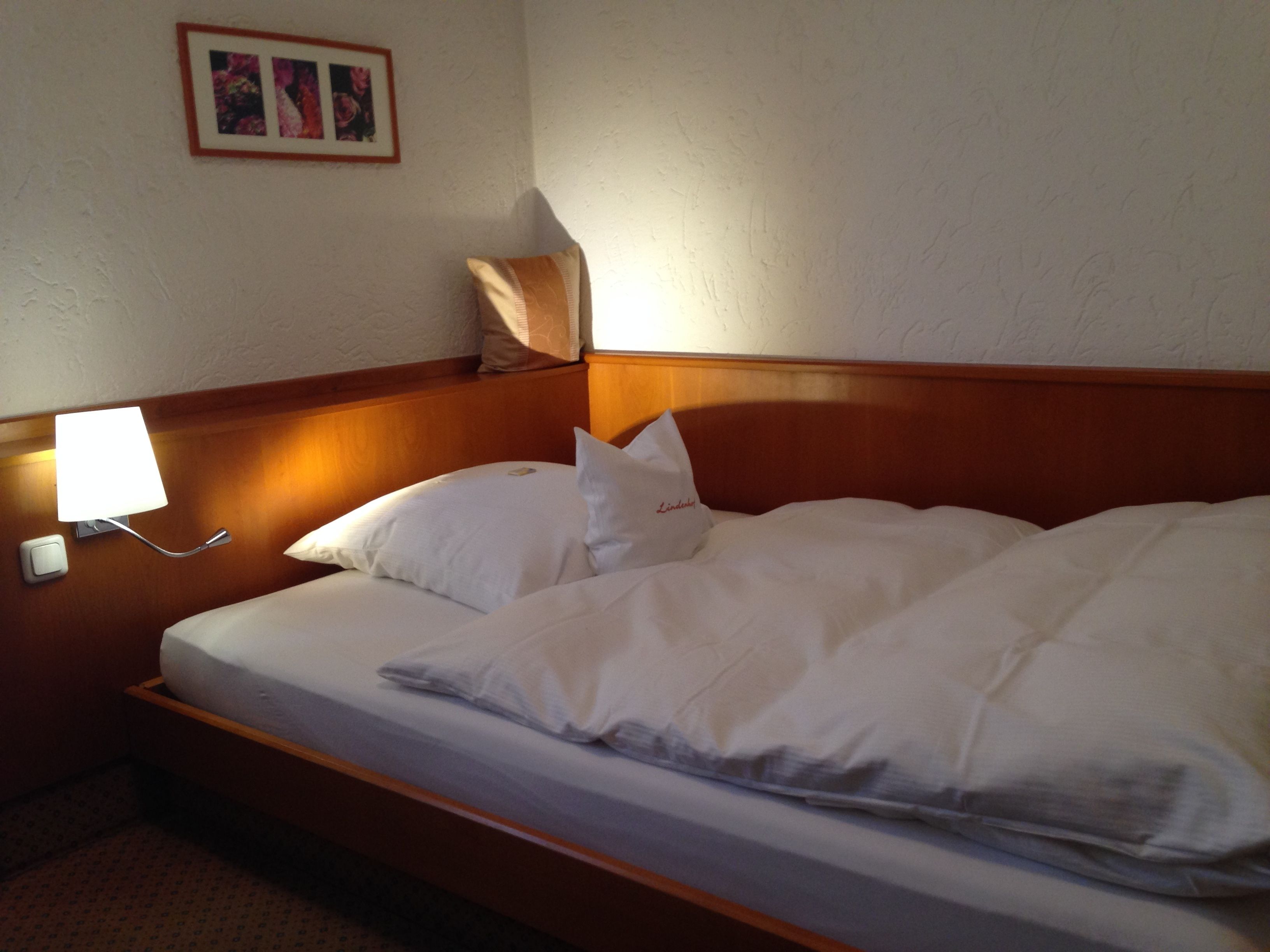 A hotel room with a wooden headboard, a bed with white linens, a bedside lamp, and a framed picture on the wall.