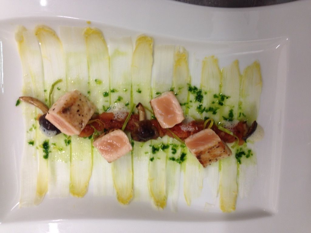 A rectangular white plate with a dish consisting of sliced fennel, pieces of salmon, and garnished with herbs.