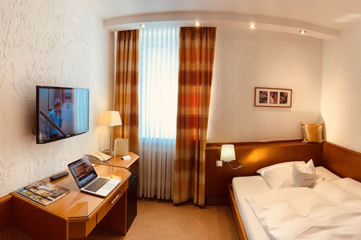 Une chambre d’hôtel avec un lit, un bureau avec un ordinateur portable, une télévision et une fenêtre avec des rideaux.