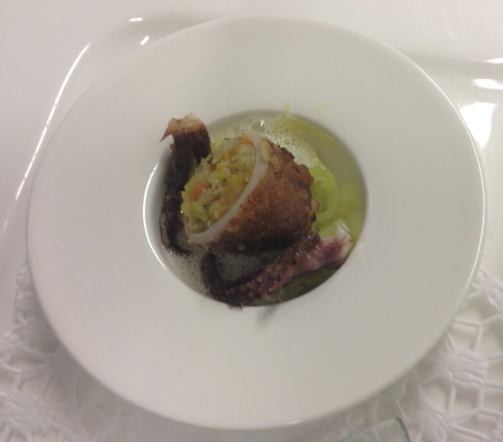 A white plate with a piece of food, possibly a croquette, on a white tablecloth.