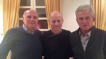 Three men standing in a room with a window and curtains.