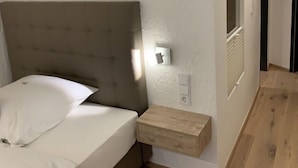 Une chambre à coucher avec un lit, une table de chevet, une lampe fixée au mur et un plancher en bois.