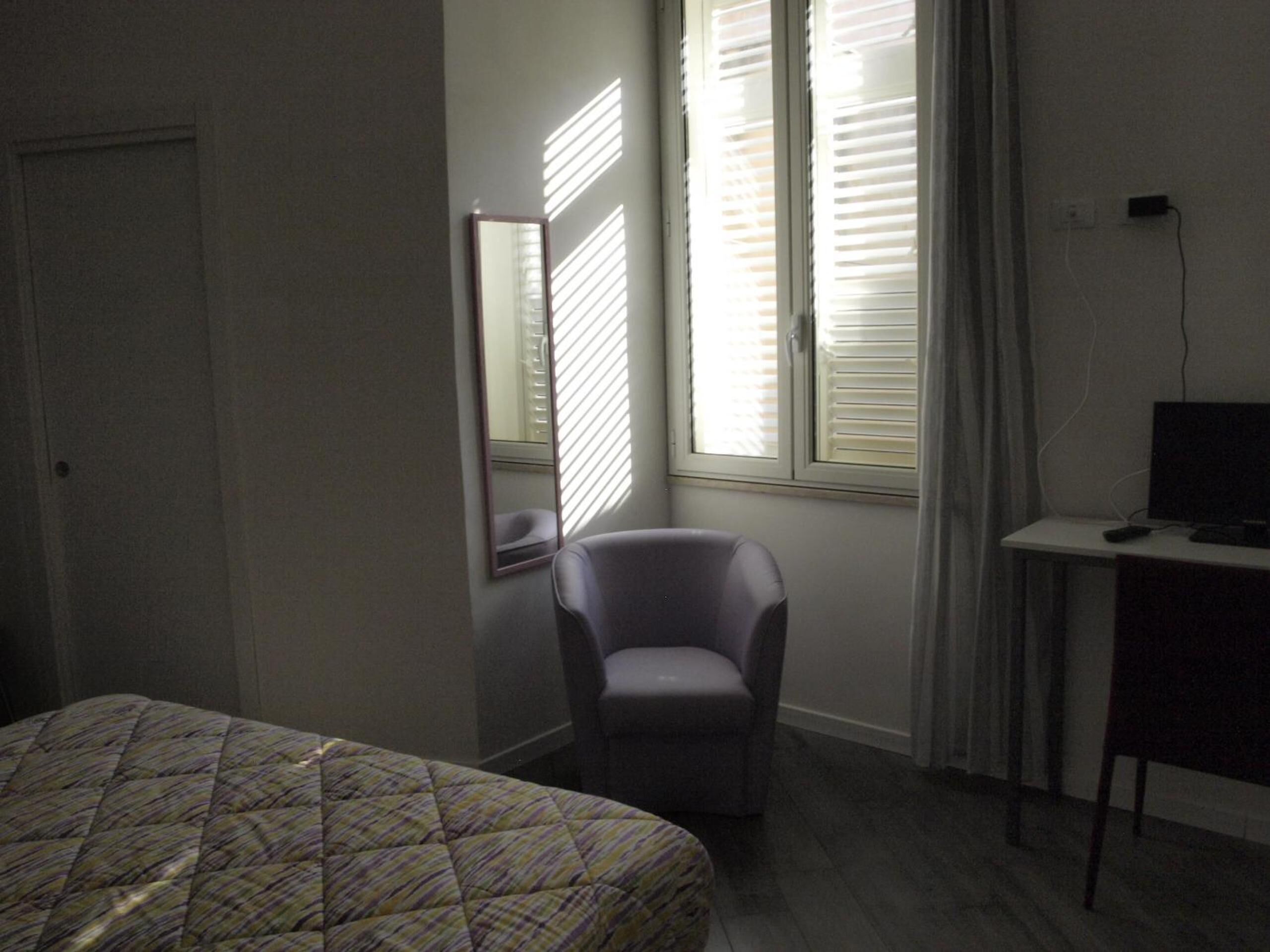 Habitación de hotel con cama, una silla, escritorio con computadora y ventana con persianas.