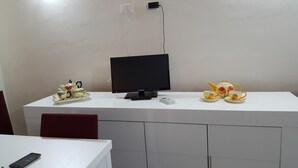 Un escritorio blanco con un monitor negro, un pequeño dispositivo blanco y un juego de té.