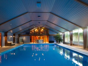 An indoor swimming pool with a wooden ceiling and a bar area in the background.