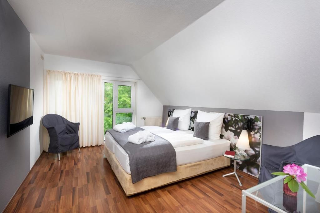 Ein modernes Schlafzimmer mit einem Bett, einem Sessel, einem Nachttisch mit Lampe und einem Vorhangfenster.