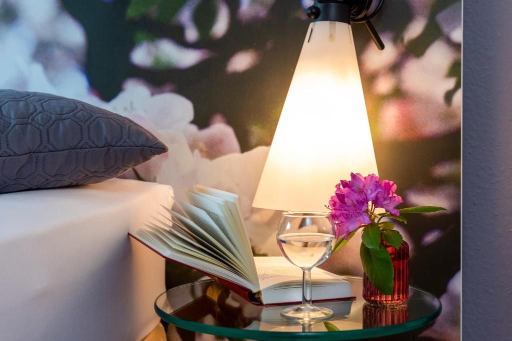 Une table de chevet avec un livre, un verre d’eau et un vase de fleurs.