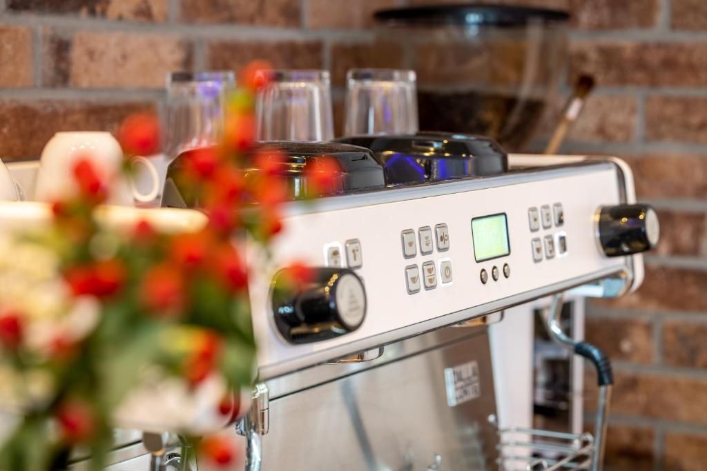 A coffee machine with a digital display and various buttons, set against a brick wall background.
