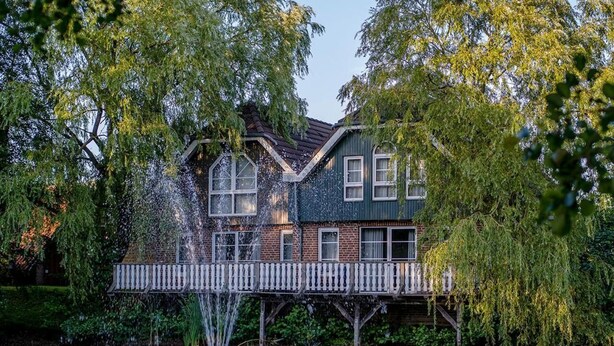 A house with a wooden deck over a body of water, surrounded by trees. - Eurostrand Resort Lüneburger Heide (Fintel)