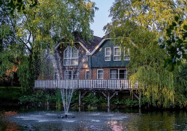 A house with a wooden deck over a body of water, surrounded by trees. - Eurostrand Resort Lüneburger Heide (Fintel)