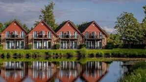 A row of red-roofed, two-story buildings with balconies, reflecting in a calm body of water. - Eurostrand Resort Lüneburger Heide (Fintel)