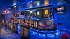 Una zona de bar con mostrador, taburetes y un letrero de neón.