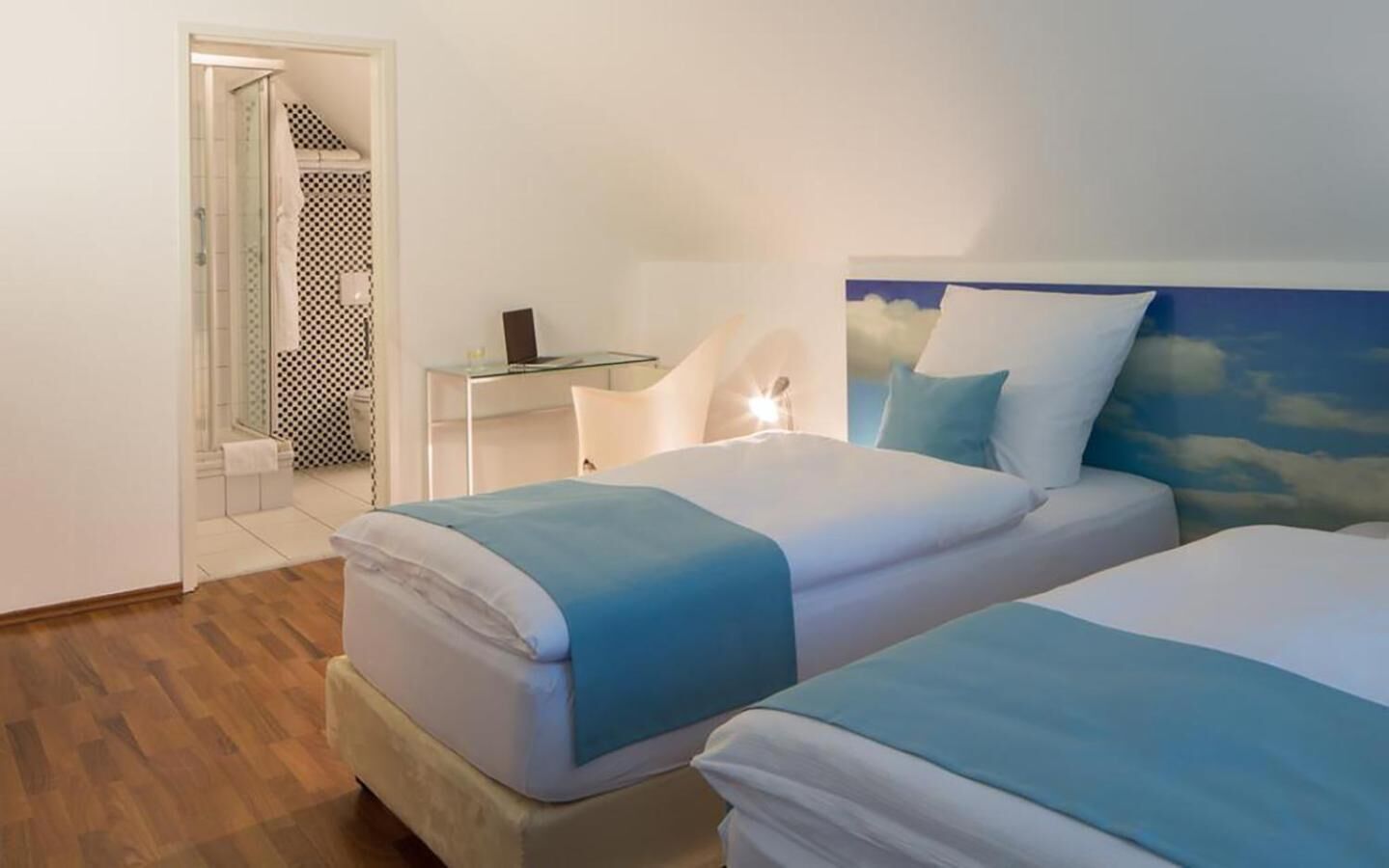 Een hotelkamer met twee bedden, een bureau en een badkamer met een douchegordijn met ruitpatroon.