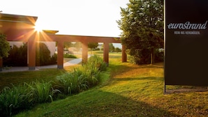 Un espacio exterior moderno con pérgola, césped y árboles.