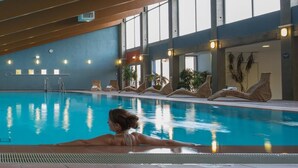 Piscina interior con agua cristalina, sillas de descanso y plantas en macetas.