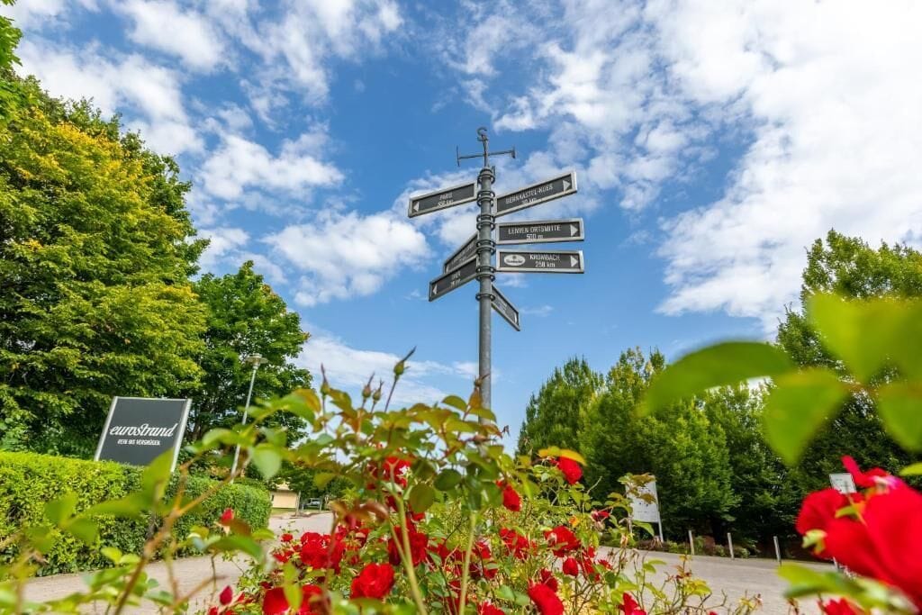 A directional signpost with multiple arrows pointing in different directions, surrounded by lush greenery and red flowers.