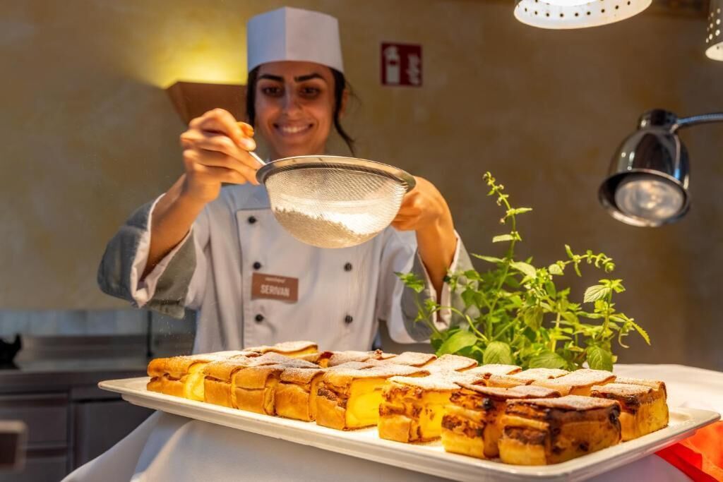 Un chef tenant une passoire au-dessus d’un plateau de nourriture, avec une plante en arrière-plan.