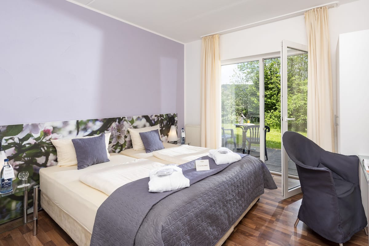 Une chambre d’hôtel équipée d’un lit, d’un bureau, d’une chaise et d’une grande fenêtre donnant sur un paysage verdoyant.