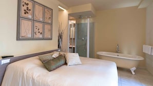 A bedroom with a large bed, a vanity with a bathtub, and framed botanical prints on the wall. - Spazio Bianco (Ivrea)