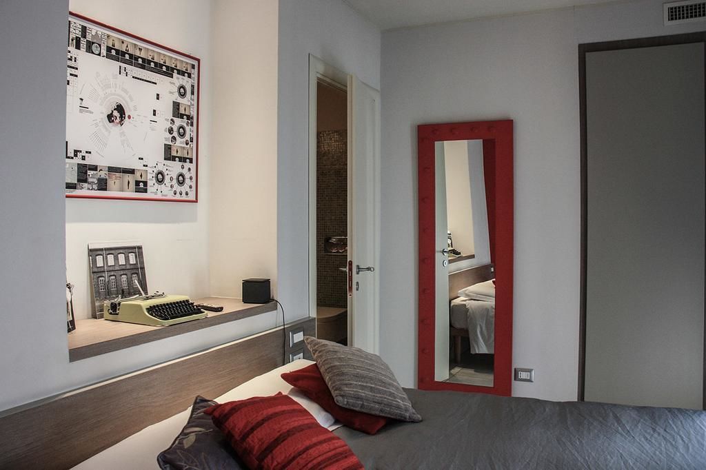 Ein modernes Schlafzimmer mit einem Bett, einem Schreibtisch mit Schreibmaschine, einem großen Poster und einem Spiegel mit rotem Rahmen.