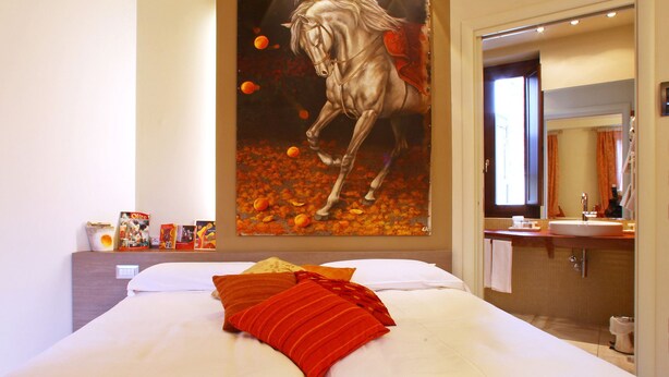 A bedroom with a large bed, a painting of a horse, and a bathroom visible through an open door. - Spazio Bianco (Ivrea)
